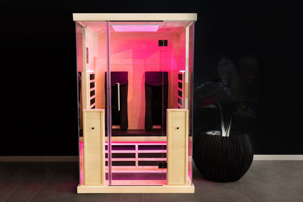 Sauna mit pinker Beleuchtung, zwei Sitzbereichen, moderner Holzoptik und minimalistischer Gestaltung.