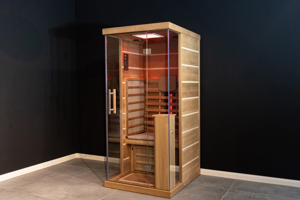 Sauna aus Holz mit Glasfront, ausgestattet mit Heizstrahlern und Holzbank.